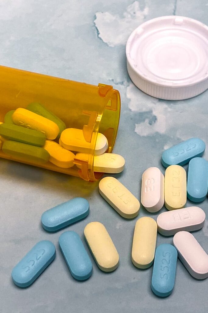 An open prescription bottle with assorted pills on a light blue background, high angle view.