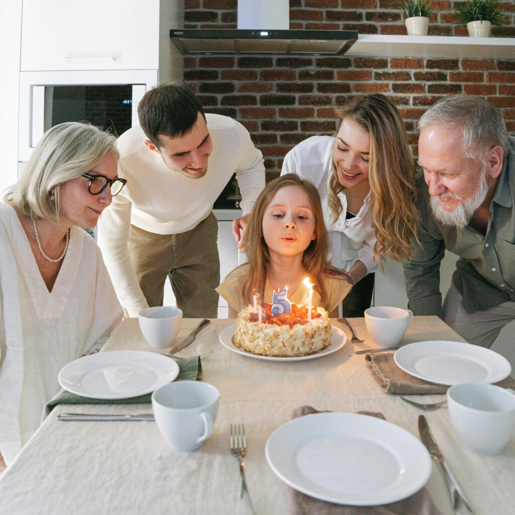 pexels photo 7922014 7922014 A young girl blows out candles on her birthday cake surrounded by family members indoors.